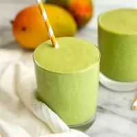 Mango kale smoothie with mangoes in background.