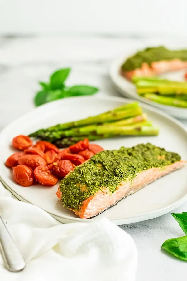 Pesto crusted salmon with veggies on a white plate.