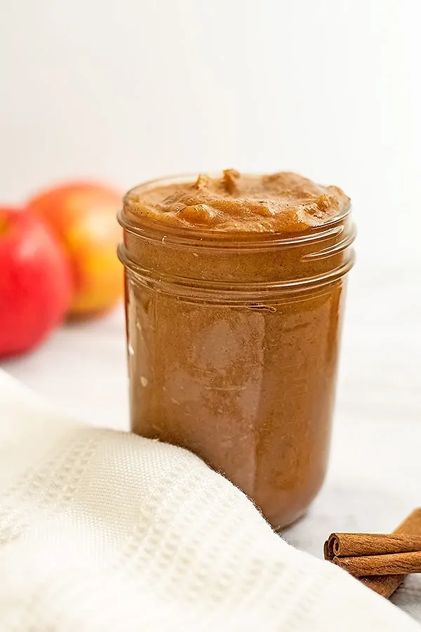 Large jar of apple butter with apples behind the jar.