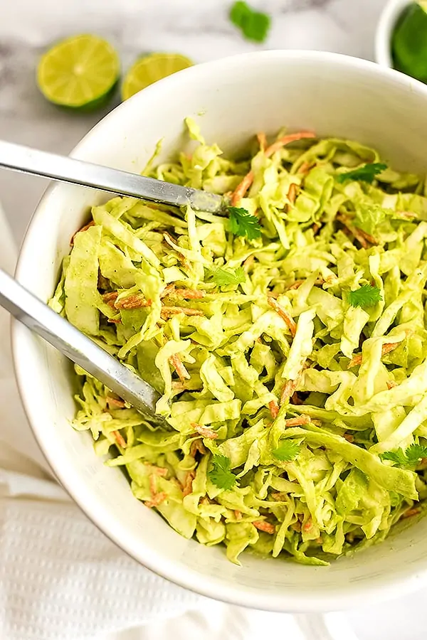 Tongs in a bowl full of creamy cilantro lime slaw. 