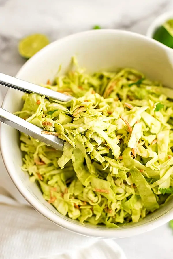 Tongs getting a serving of creamy cilantro lime coleslaw.