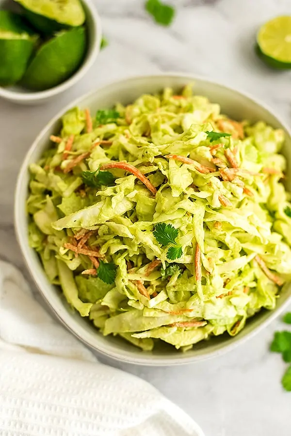 Creamy cilantro lime slaw in a bowl with limes in background.