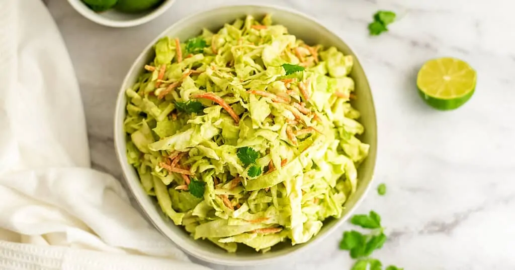 White bowl filled with cilantro lime slaw, limes on the side.