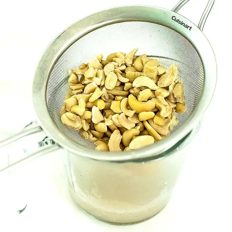 Cashews in a mesh strainer over a measuring cup.