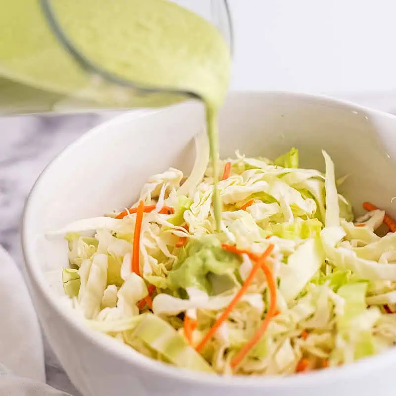 Cilantro lime dressing being poured over slaw.