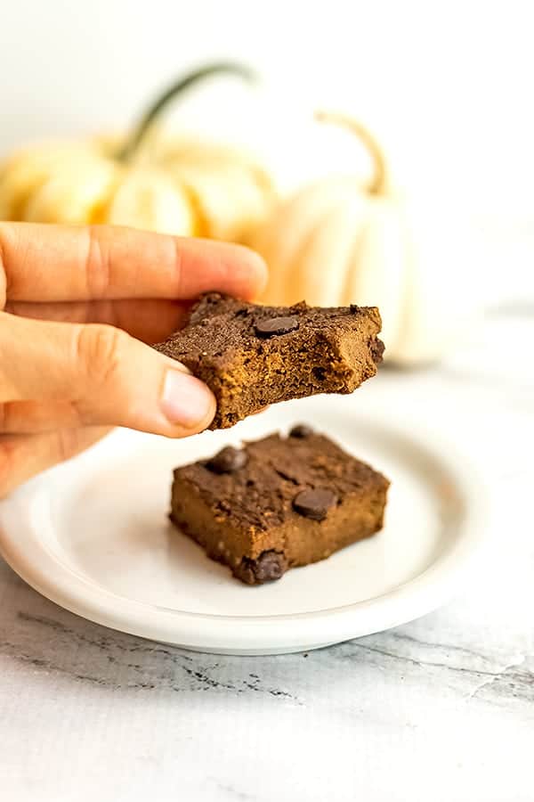 Hand holding a pumpkin brownie with a bite taken out of it. 