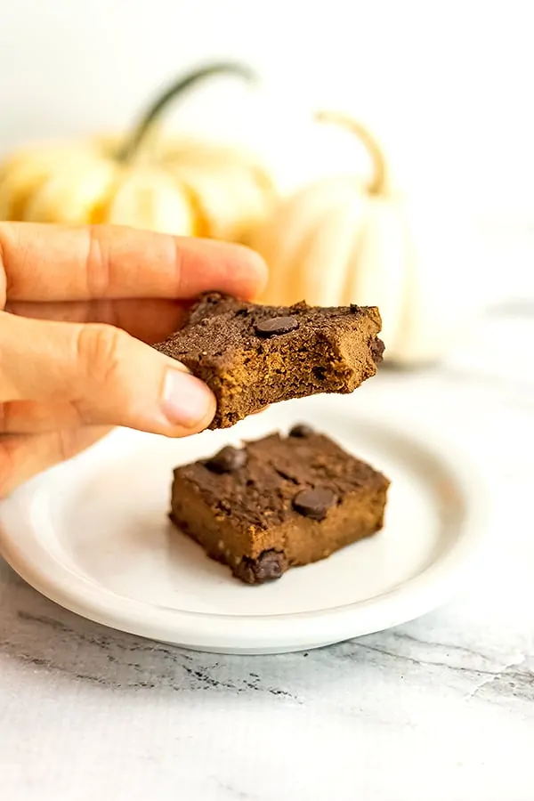 Hand holding a pumpkin brownie with a bite taken out of it. 