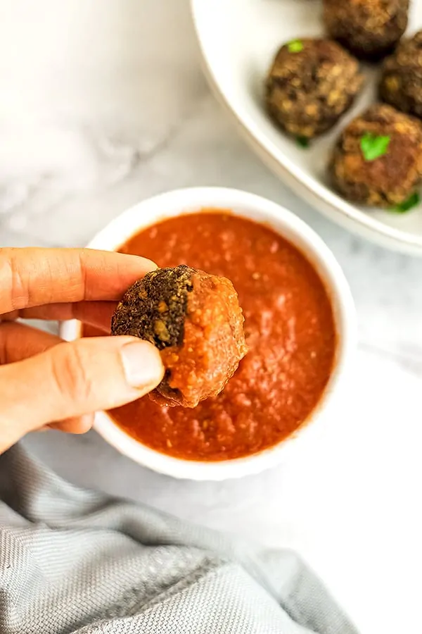 Hand dipping a vegan meatball in red sauce.