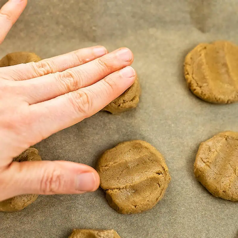 Hand pressing down peanut butter cookie dough on baking sheet.