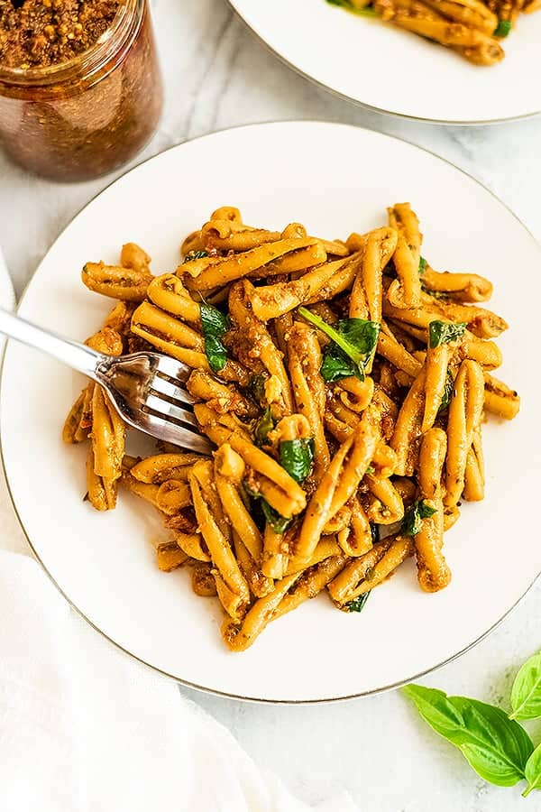 Fork picking up a bite of red pesto pasta.