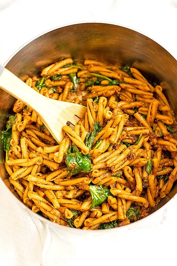 Wooden spoon in pot with red pesto pasta.