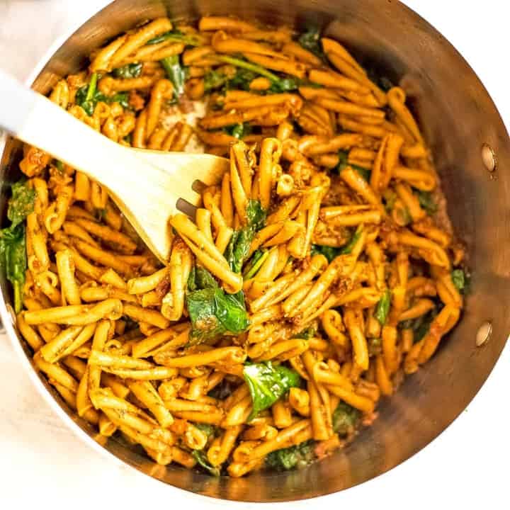 Pot filled with sundried tomato pesto pasta with wooden spoon.
