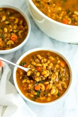 Bowl of pasta fagioli with a soup taking a bite.