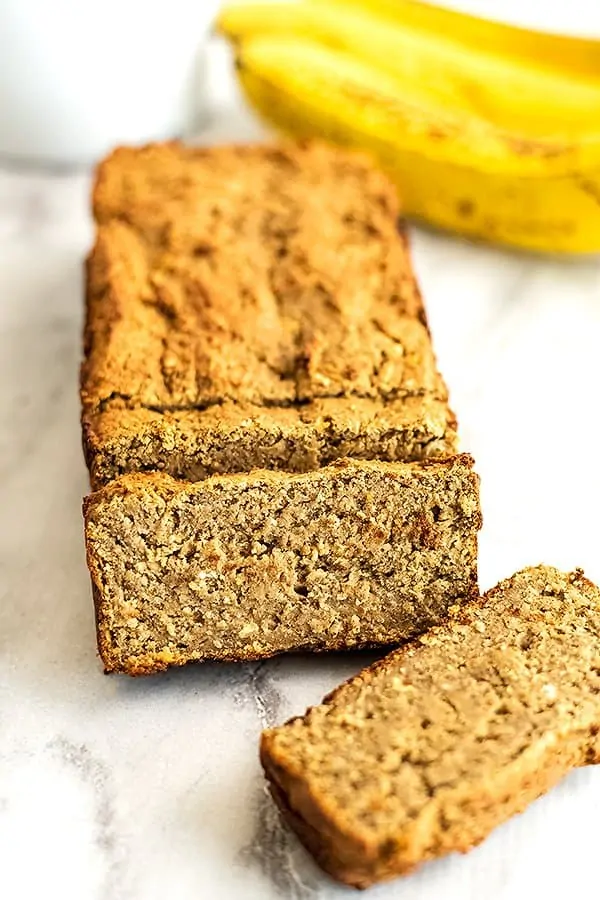 Vegan banana bread sliced with bananas in background.