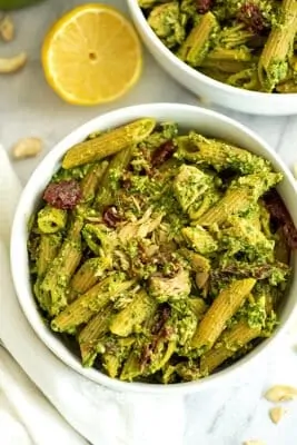 Tuna pesto pasta in a white bowl with lemons in background.