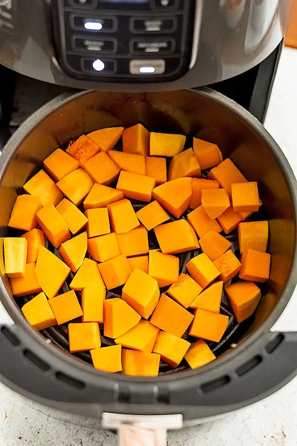 Air fryer basket filled with butternut squash cubes before cooking.