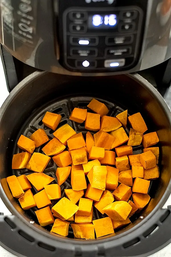 Air fryer basket filled with butternut squash cubes during cooking.