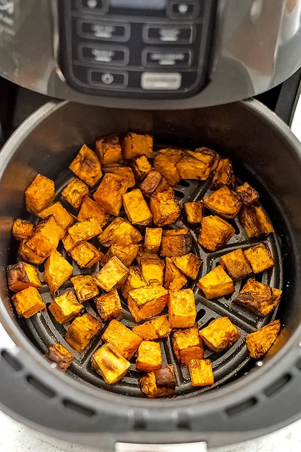 Air fryer basket filled with butternut squash cubes after cooking.