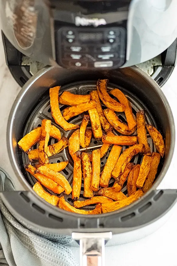 Air fryer basket filled with butternut squash fries.