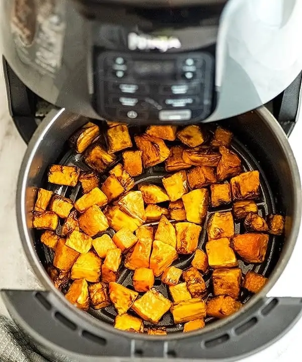 Air fryer basket filled with butternut squash cubes.