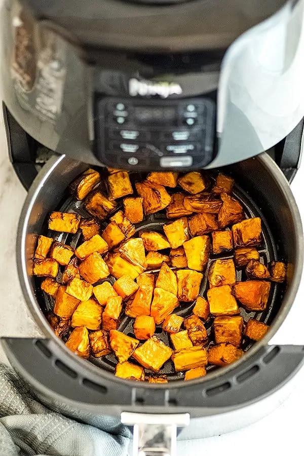 Air fryer basket filled with butternut squash cubes.