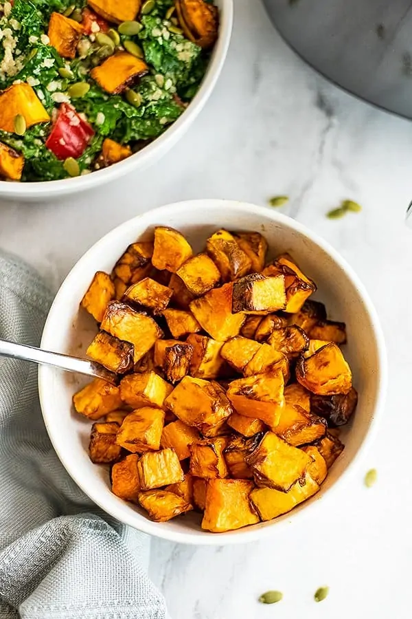 Bowl with air fryer butternut squash cubes and salad in background.