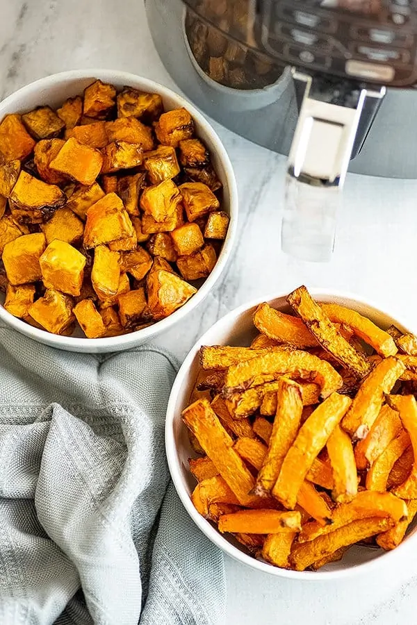 One bowl filled with air fryer butternut squash fries, other with cubes.