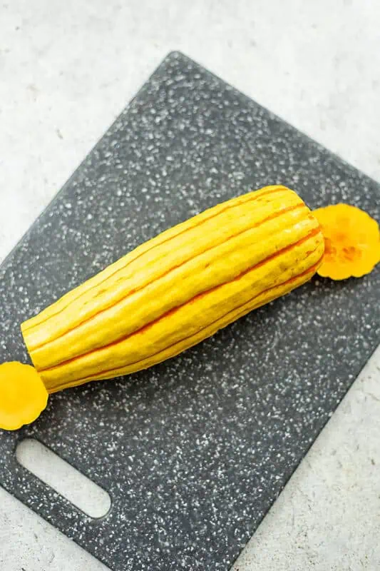 Top and bottom of the delicata squash have been cut off, it's resting on a cutting board.