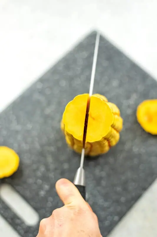 Hand holding a knife that is slicing into a delicata squash.