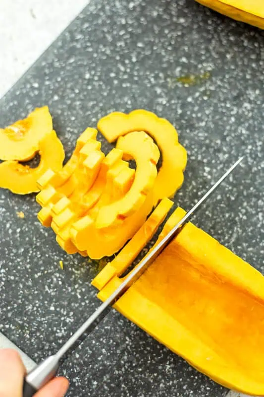 Knife slicing delicata squash into thin pieces.