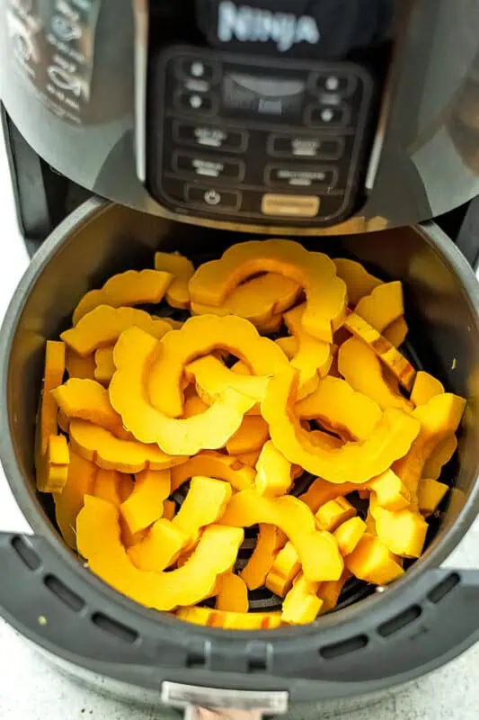 Delicata squash slices in air fryer before cooking.
