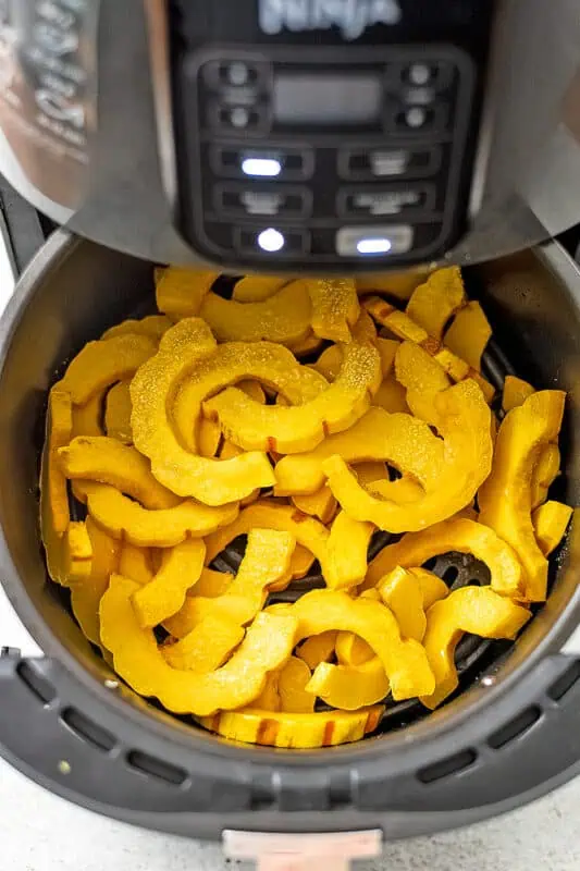 Delicata squash slices in air fryer before shaking.