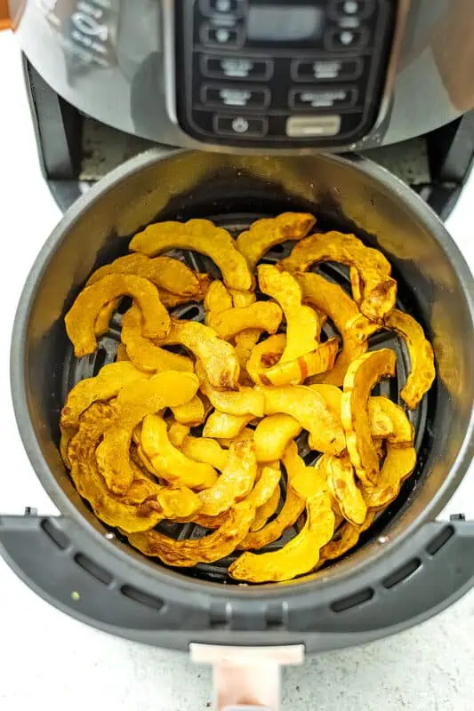 Cooked delicata squash slices in air fryer basket
