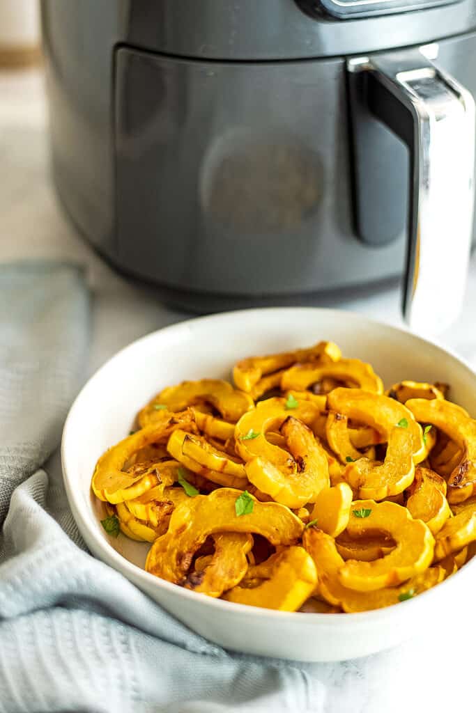 Air fryer in background of bowl filled with delicata squash.