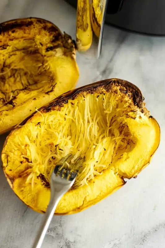 Fork dragging across spaghetti squash to release noodles.
