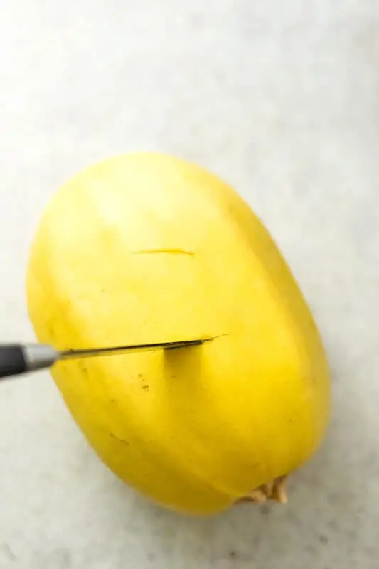Knife piercing the skin of spaghetti squash.