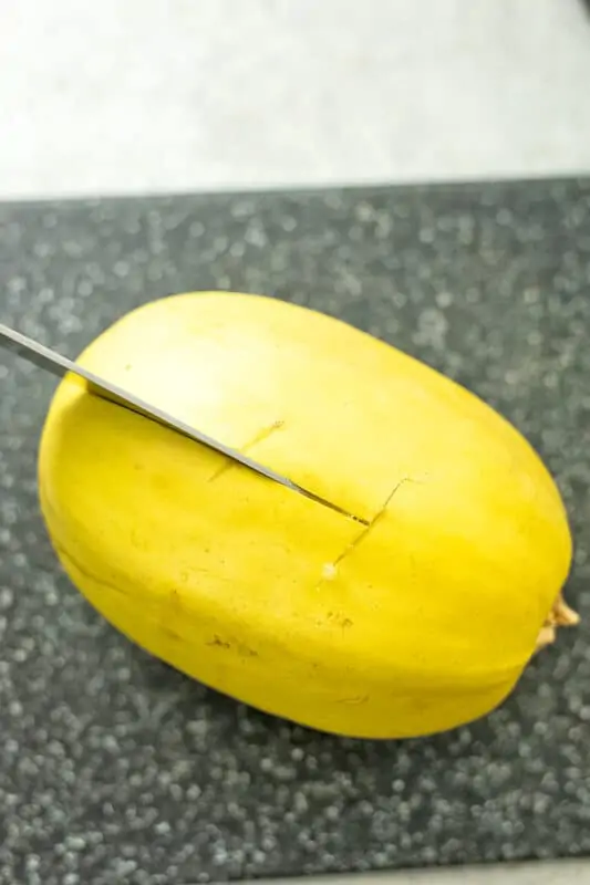 Knife slicing spaghetti squash in half.