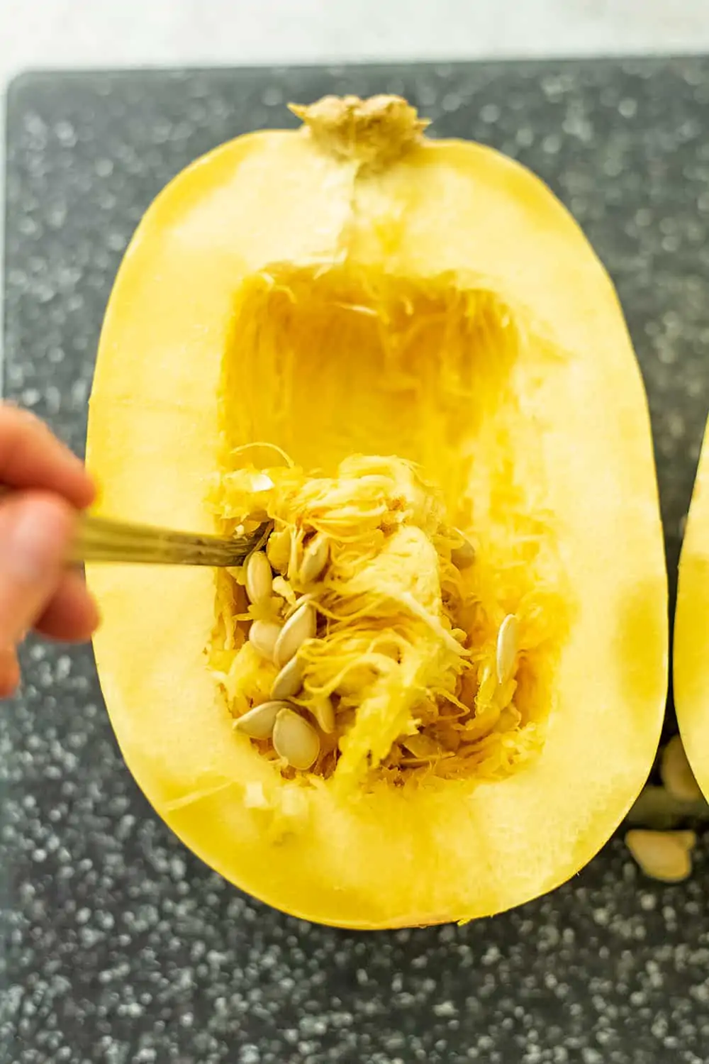 Spoon removing the seeds of a spaghetti squash.