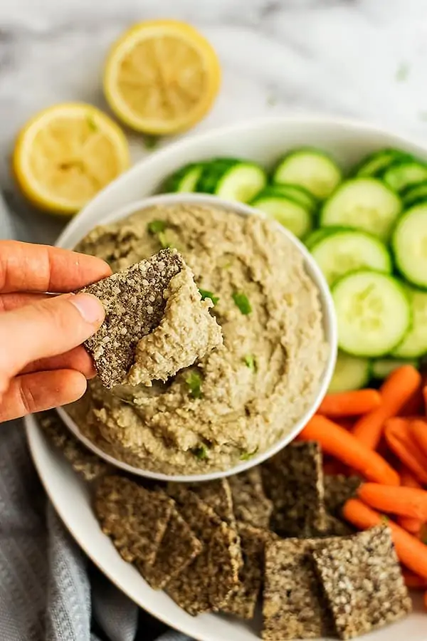 Flax cracker being dipped in hummus.