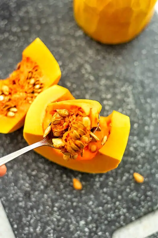 Spoon removing the seeds from a butternut squash.