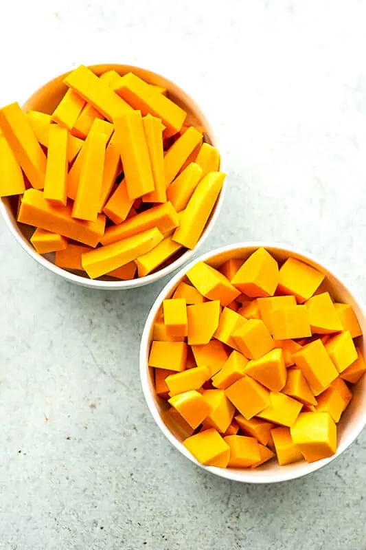 Butternut squash cut into cubes and fries in white bowls.