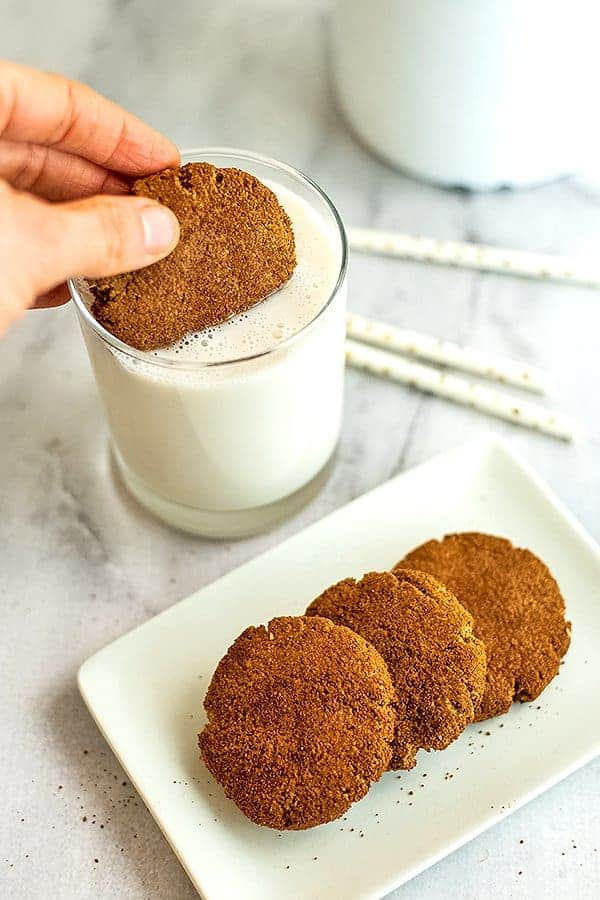Hand dipping paleo molasses cookie in glass of milk.