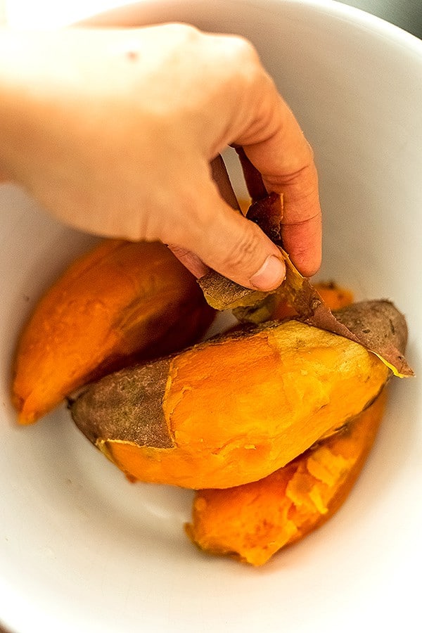 Hand peeling skin from cooked sweet potatoes.
