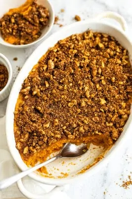 Oval casserole dish filled with sweet potato casserole with a spoon.