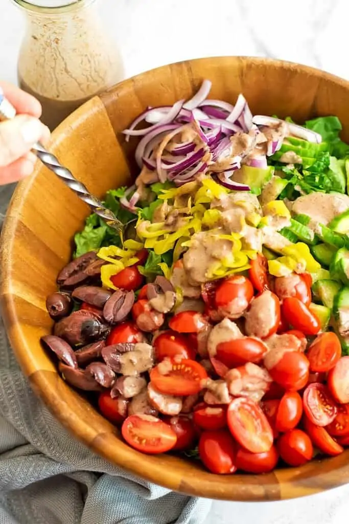 Greek salad with dressing drizzled over top before stirring.