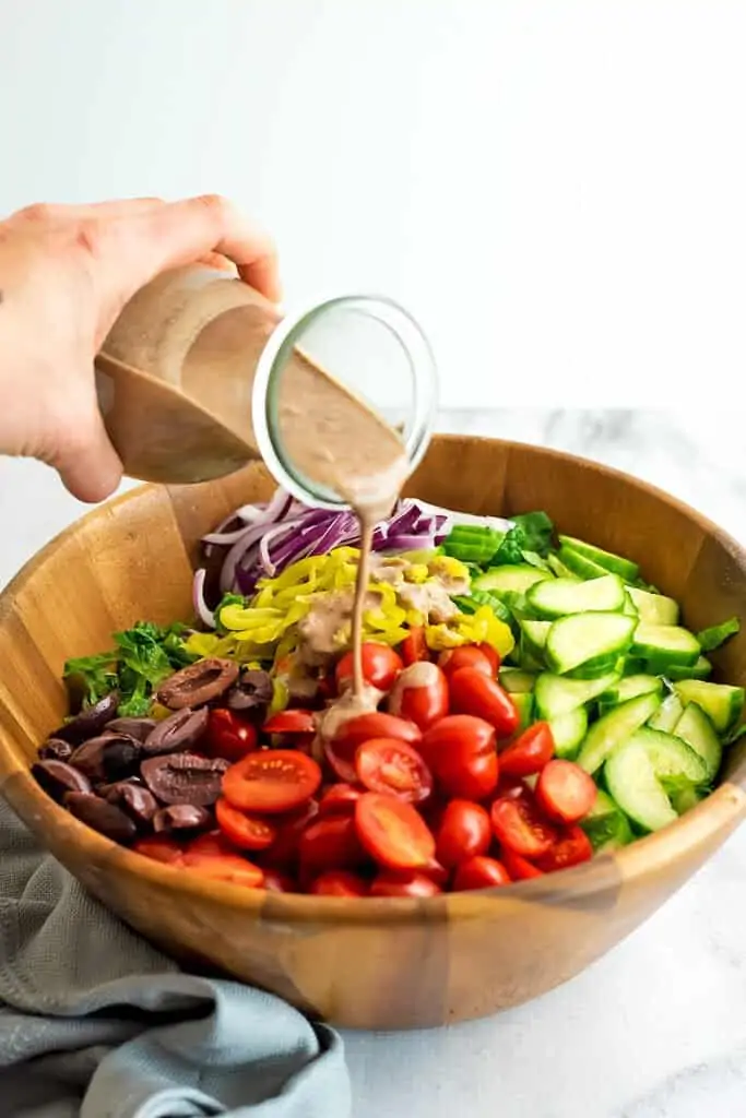 Kalamata olive dressing being poured over greek salad.