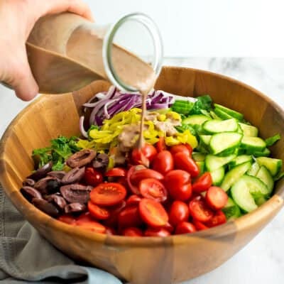 Greek salad in a wooden bowl with dressing being poured over the salad.