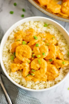 Bang bang shrimp on cauliflower rice in a white bowl.