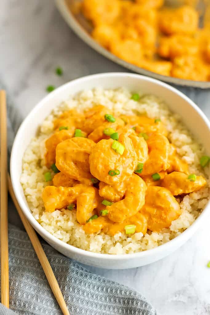 Bowl filled with bang bang shrimp on top of cauliflower rice with chopsticks.