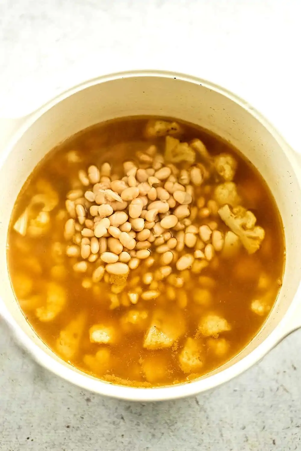 Pot filled with soup, beans being added to the soup.